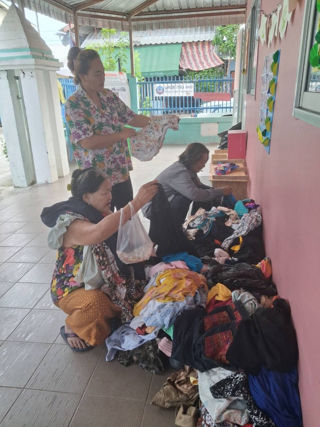 Women selecting donated clothing items arranged along a wall in the slum community.