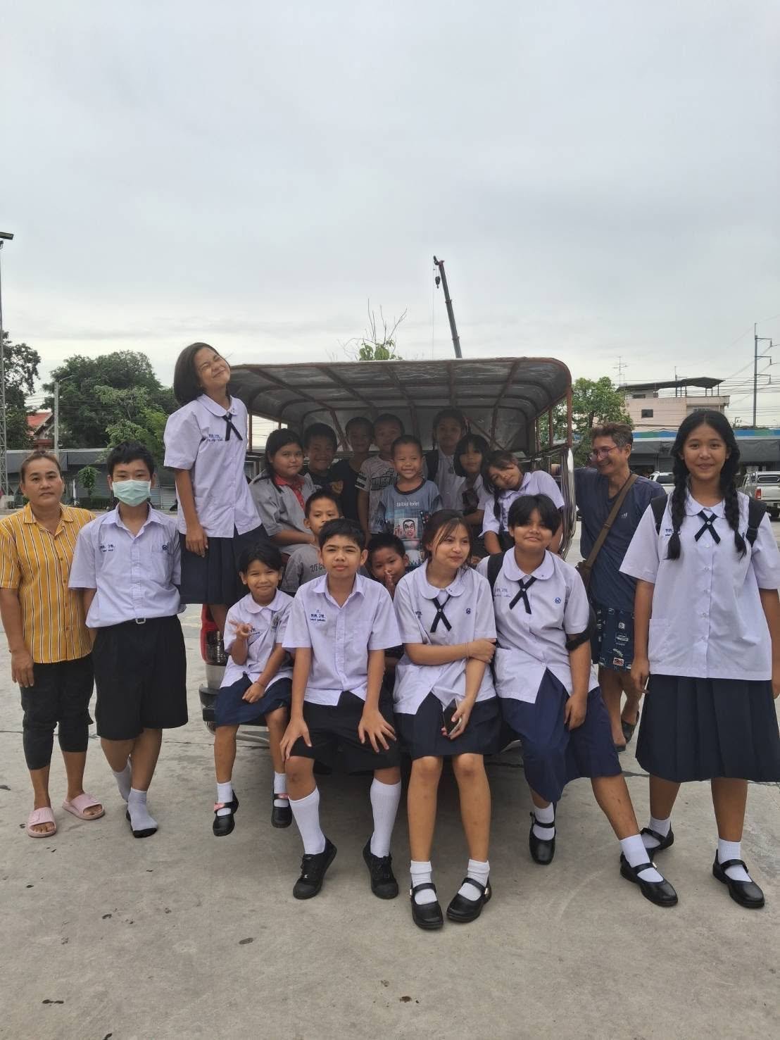 A larger group of school children and community members gathered around school transport support.