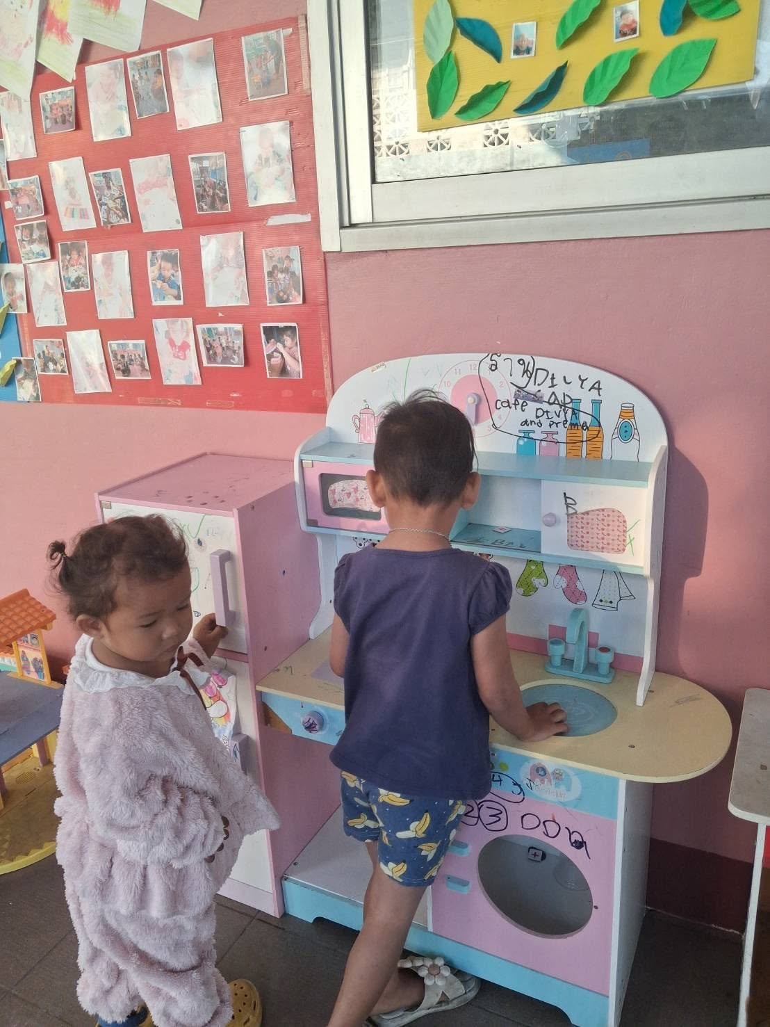 Young children playing near a donated wooden toy kitchen in the community center.