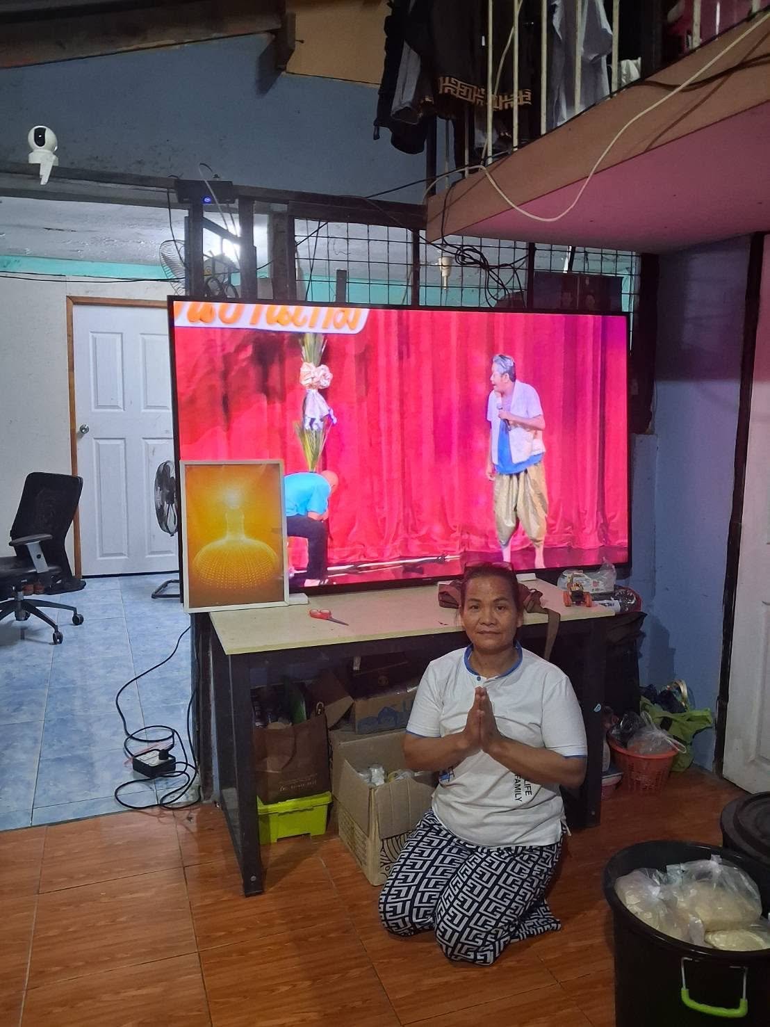 A woman in the slum community offering thanks with hands together beside a donated large television.